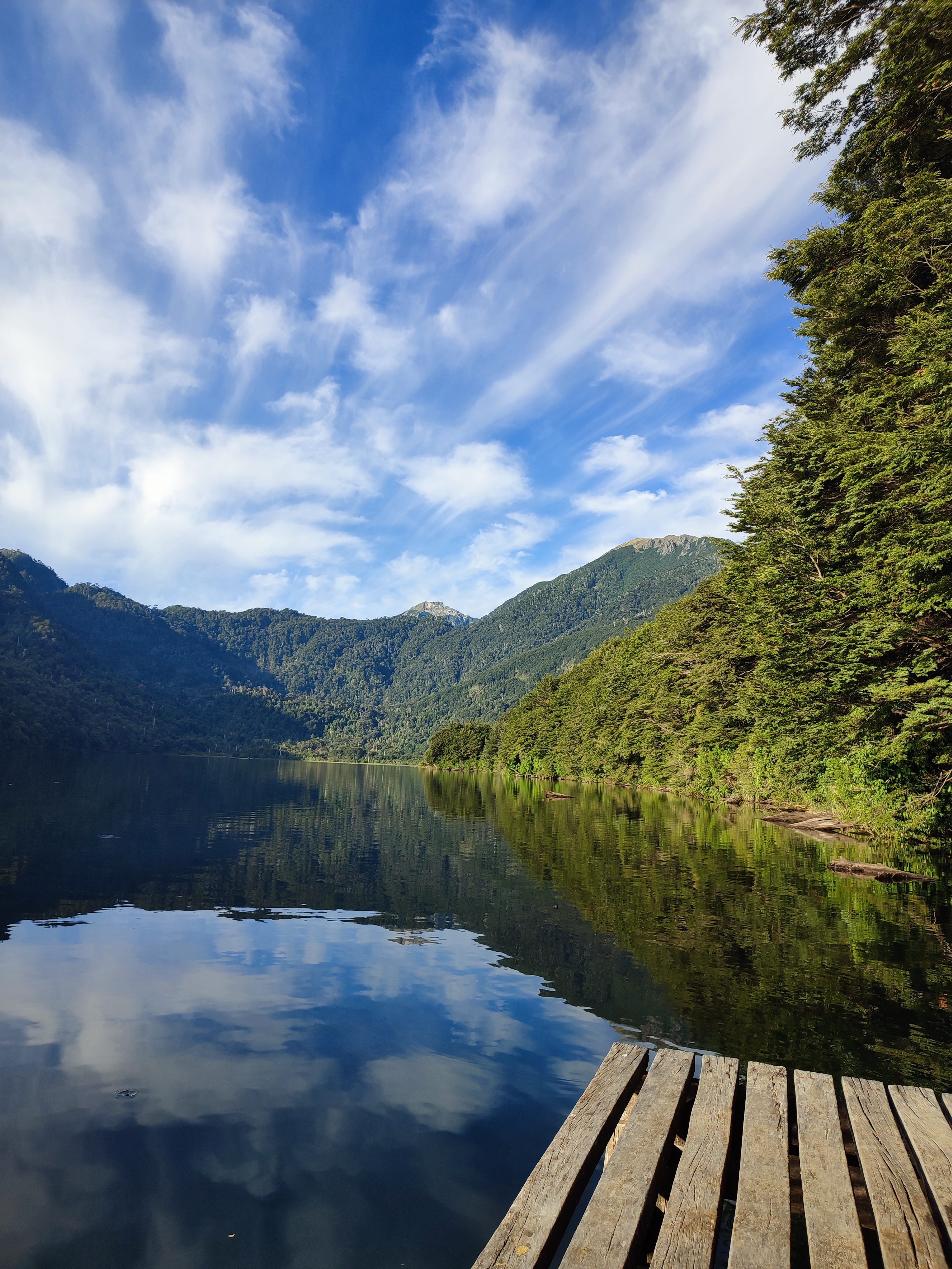 Vista del Lago Tinquilco desde un muelle de madera con cielo azul y montañas reflejadas